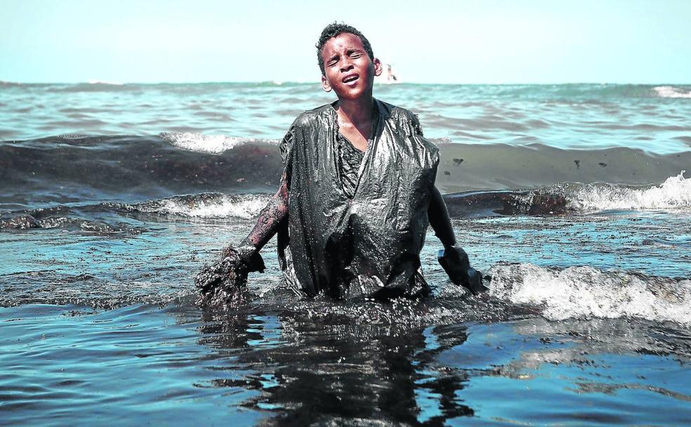 El joven Everton Miguel dos Anjos, saliendo del agua envuelto en petróleo.