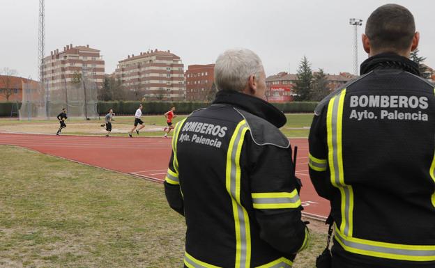 Dos bomberos contemplan este viernes a los aspirantes durante la prueba de carrera de resistencia en el Campo de la Juventud. 