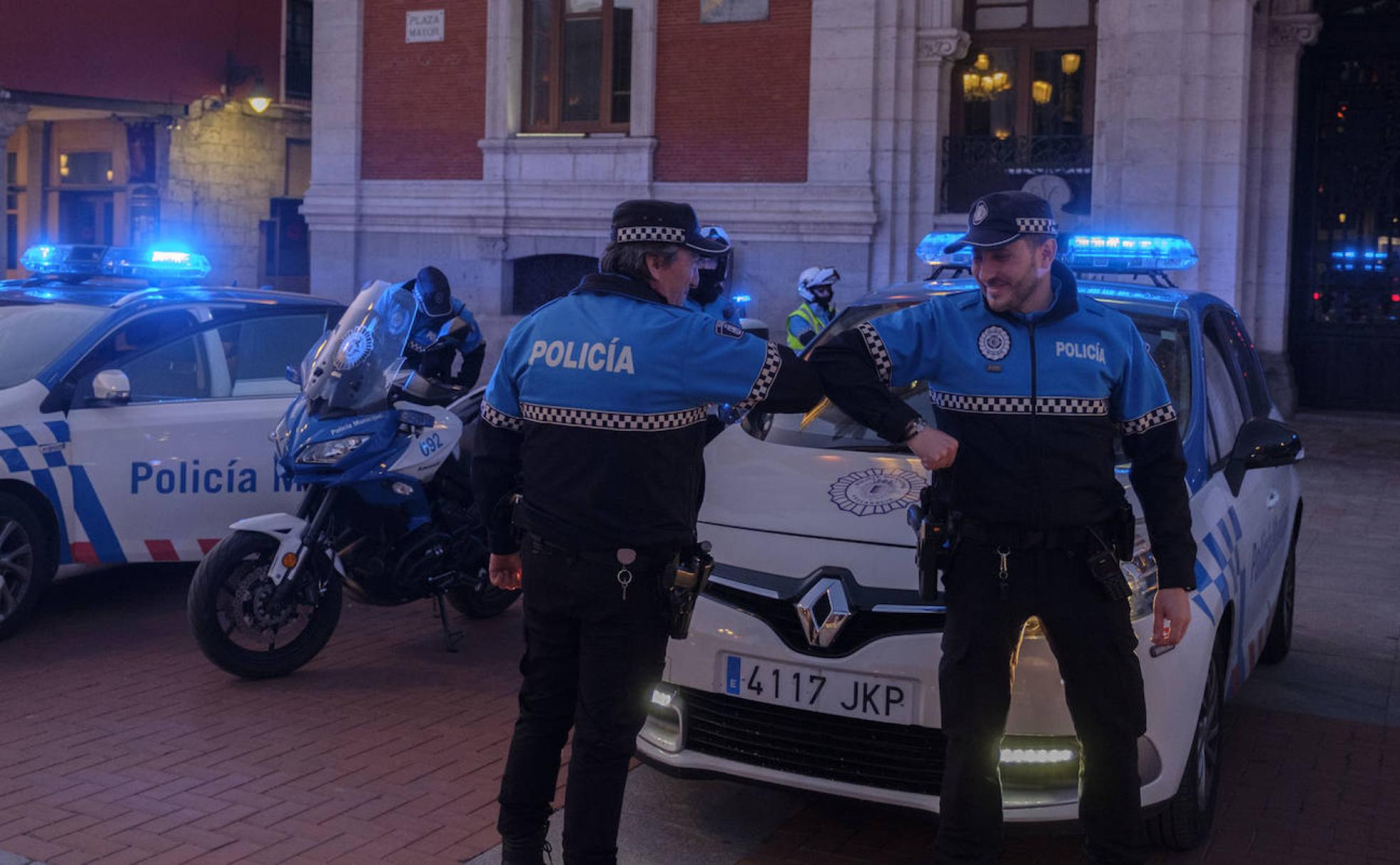 Dos agentes municipales se saludan con el codo durante el homenaje a los servicios sociales en la Plaza Mayor de Valladolid. 