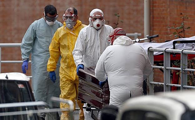 Los operarios de una funeraria trasladan el féretro de un fallecido por coronavirus.