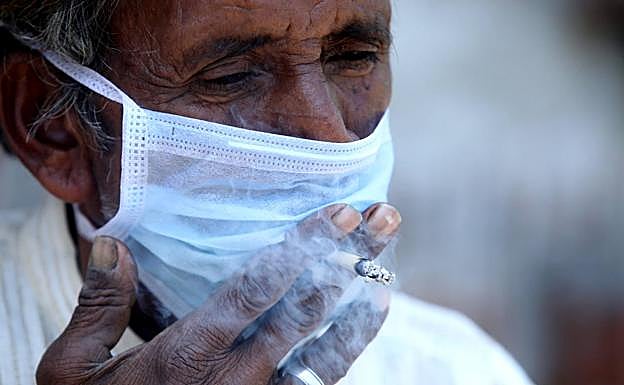 Un hombre fuma a través de la mascarilla en la India. 