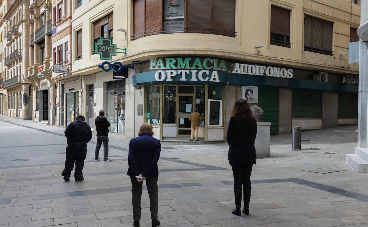 Clientes guardando cola con la distancia recomendada a las puertas de una farmacia en Salamanca. 