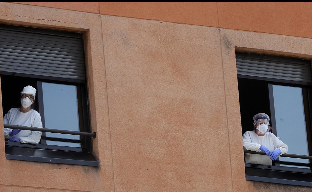 Dos miembros de la plantilla de la residencia Parquesol, con nuevos EPI, se asoman por las ventanas del centro. 