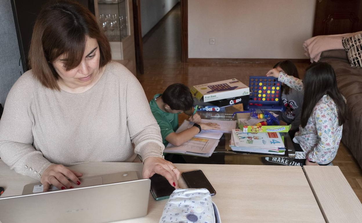 Una madre trabaja desde casa mientras sus hijos estudian al lado. 