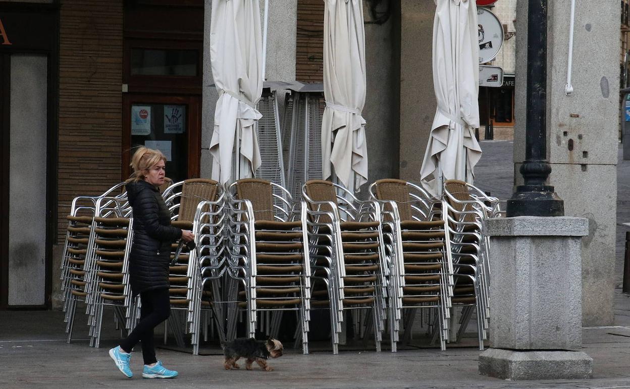 Una mujer pasea con su perro ante una terraza recogida durante la pandemia en Segovia. 