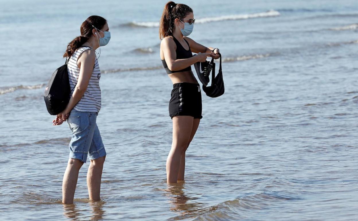 Dos jóvenes se protegen con mascarilla a la orilla del mar.