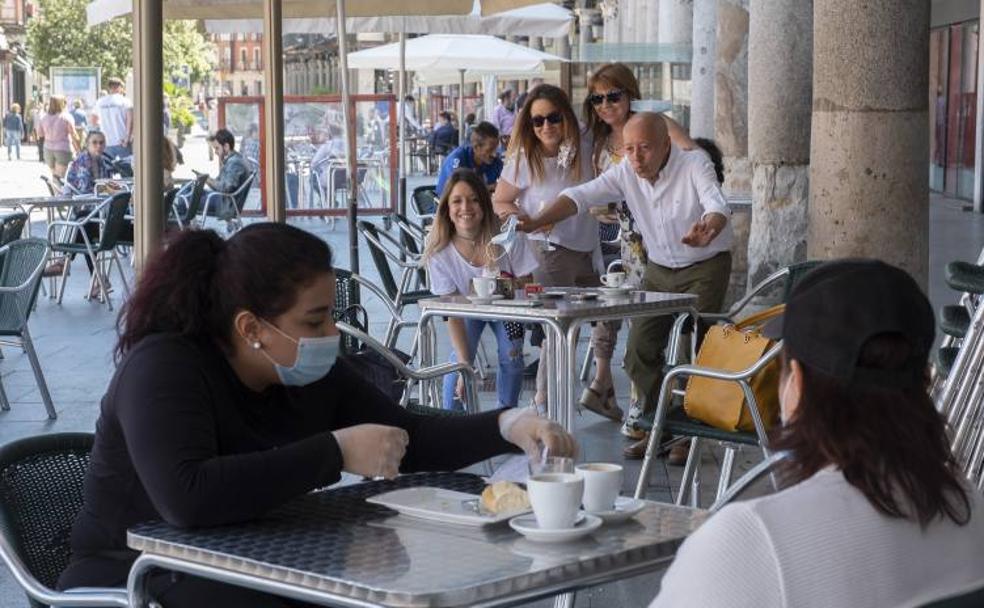 Vista desde una de las mesas del Café del Norte de dos jóvenes que conversan mientras toman un café. Al fondo, una familia posa en la que fue su primera fotografía tras el confinamiento. 