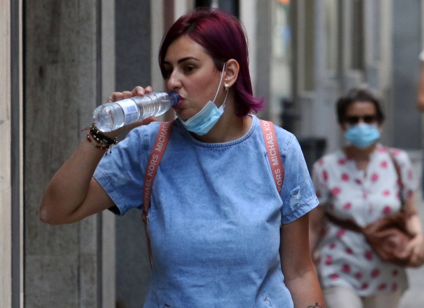 Una mujer bebe agua por la calle. 