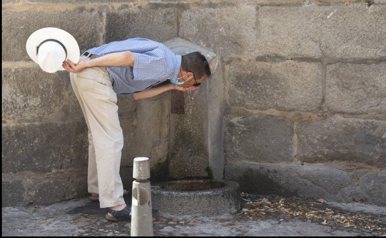 Un hombre se refresca en una fuente de la ciudad. 