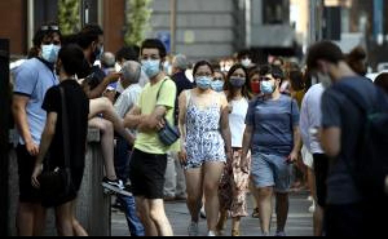 Varios jóvenes caminan con mascarilla por una calle del centro de Madrid. 