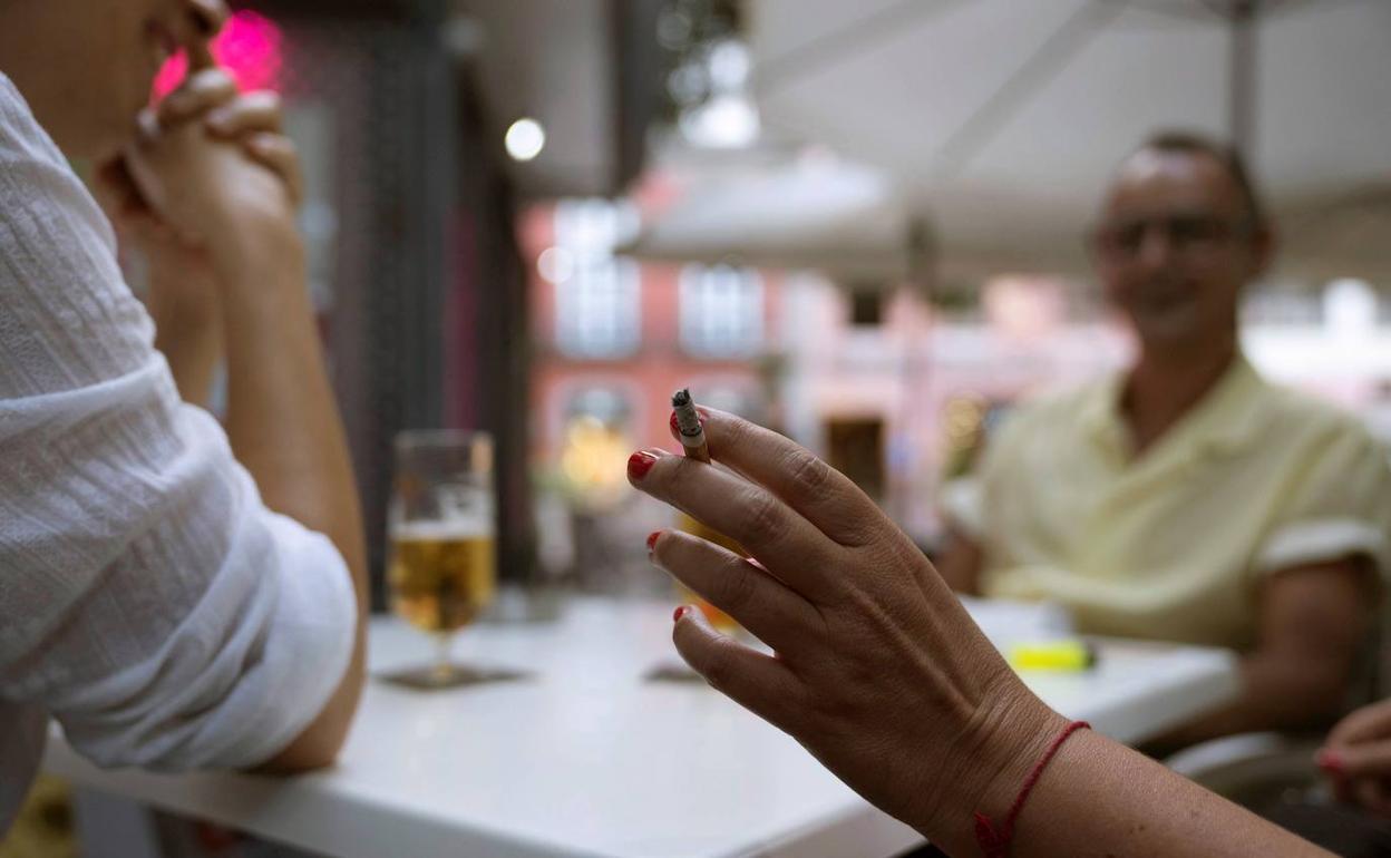 Un grupo de gente toma algo y fuma en una terraza de un bar. 