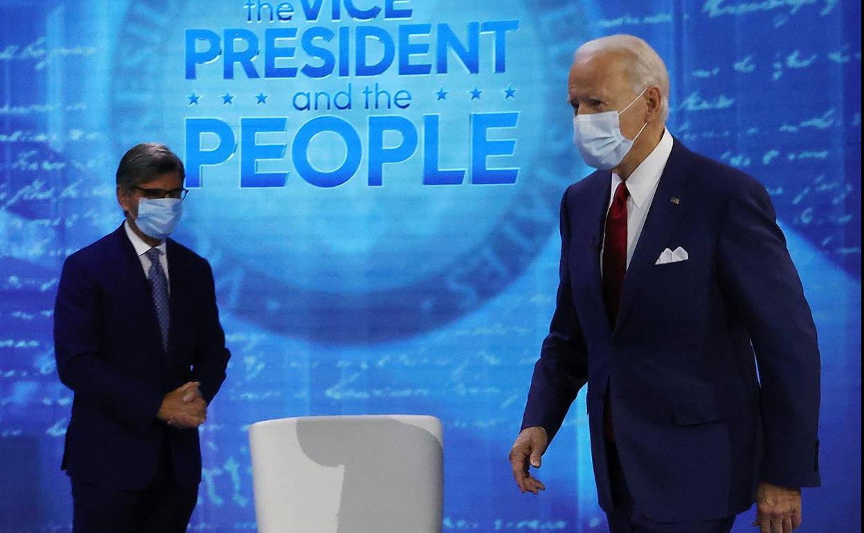 Joe Biden se acerca a su silla ante la mirada del moderador del programa en Filadelfia.