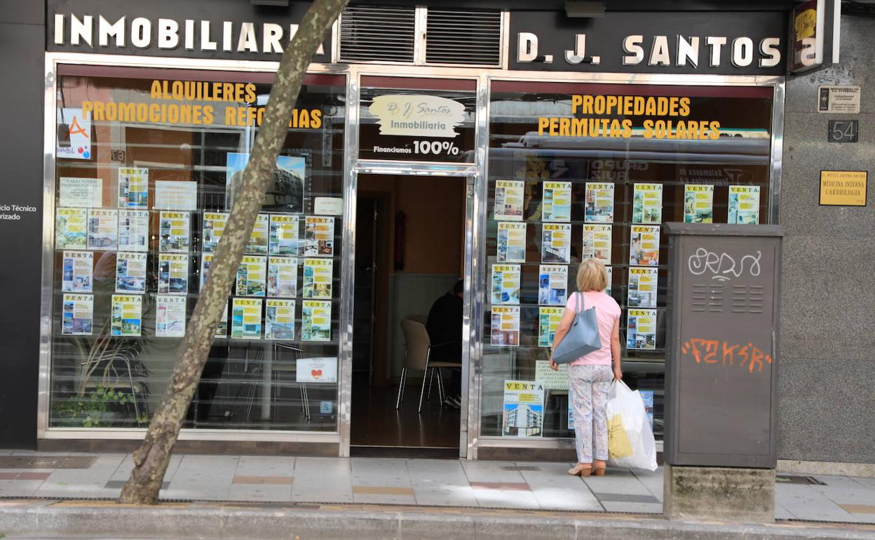 Una ciudadana lee detenidamente los anuncios de venta y alquiler de pisos publicitados en el escaparate de una inmobiliaria.