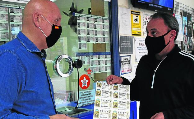 El lotero Luis Galindo (izquierda) despacha un billete a un cliente. 