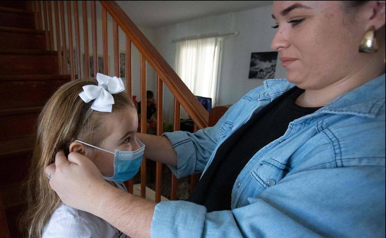 Una madre coloca la mascarilla a su hija.