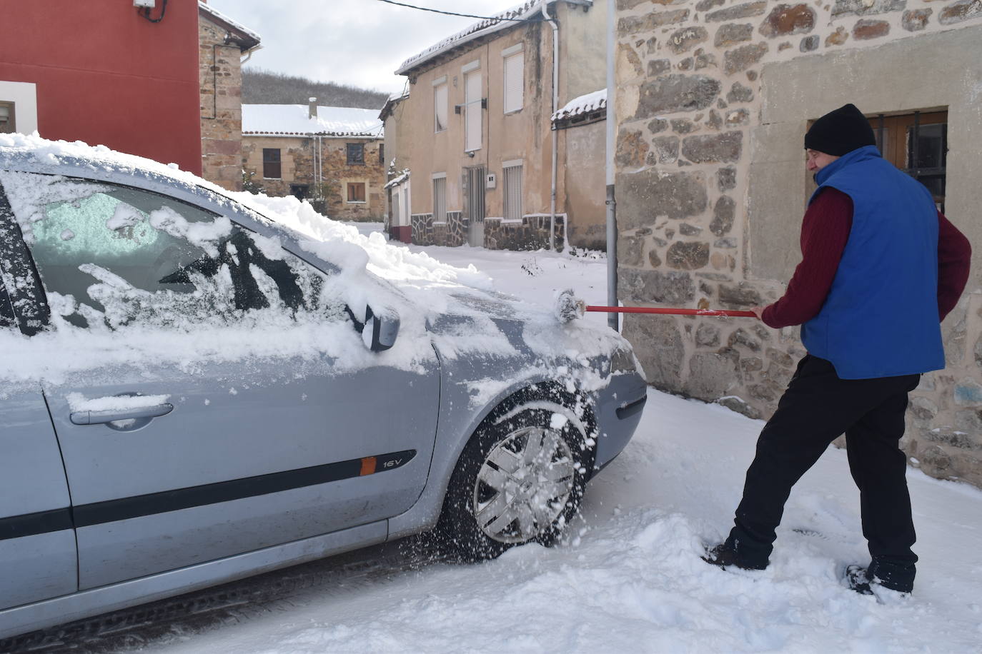 Un hombre retira la nieve de su coche en Porquera de Santullán.