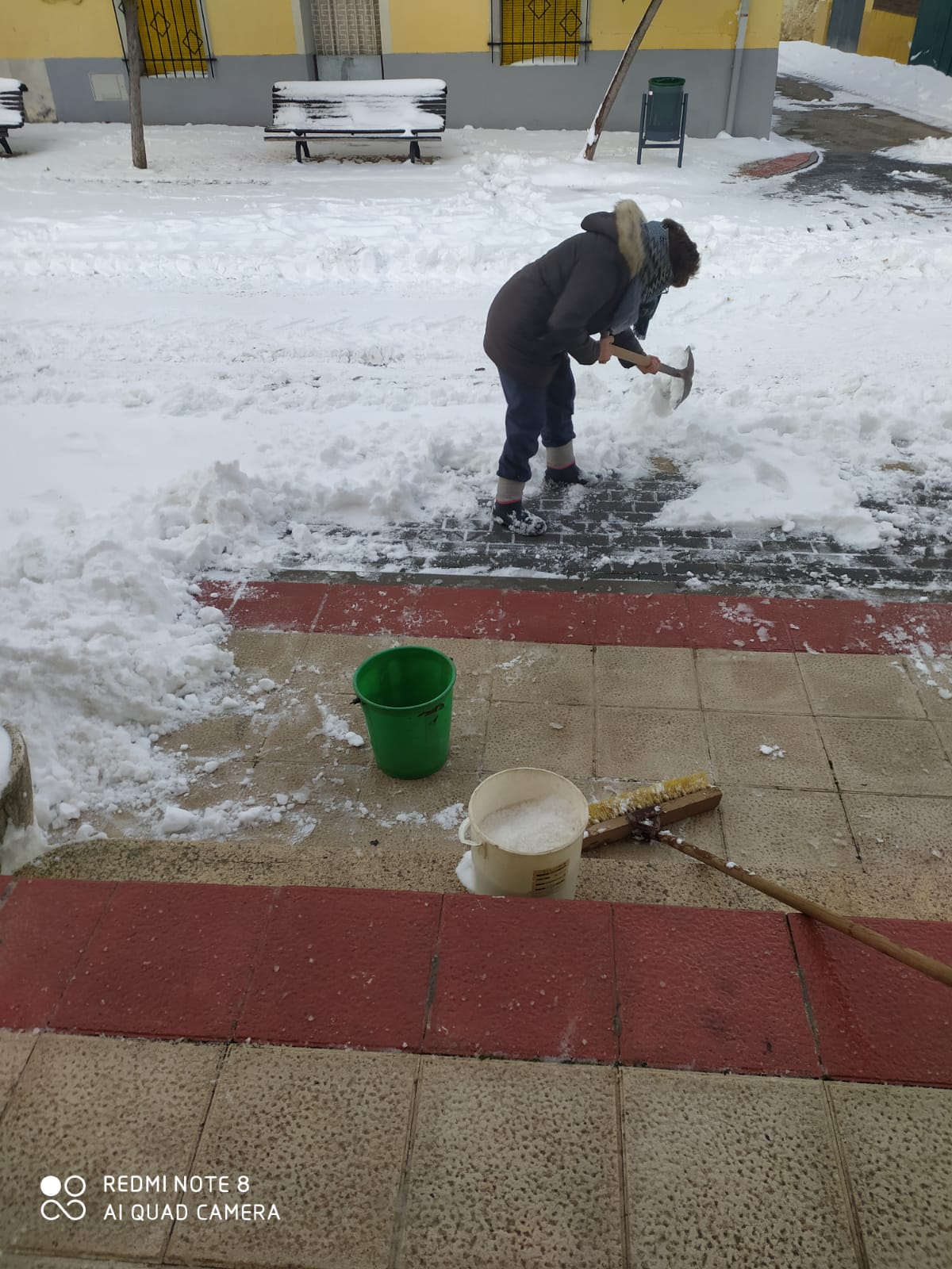 La alguacil de Castrodeza eliminando el hielo de la puerta del Ayuntamiento.