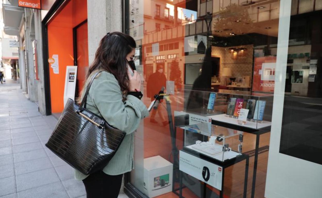 Una joven habla por teléfono frente al escaparate de una tienda de móviles.