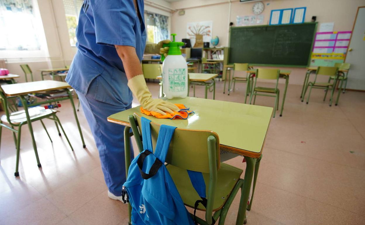Una limpiadora desinfecta un aula en un colegio.