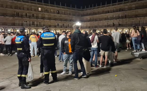 Un policía identifica a un joven en la Plaza Mayor mientras otro lleva una bolsa con bebidas requisada.