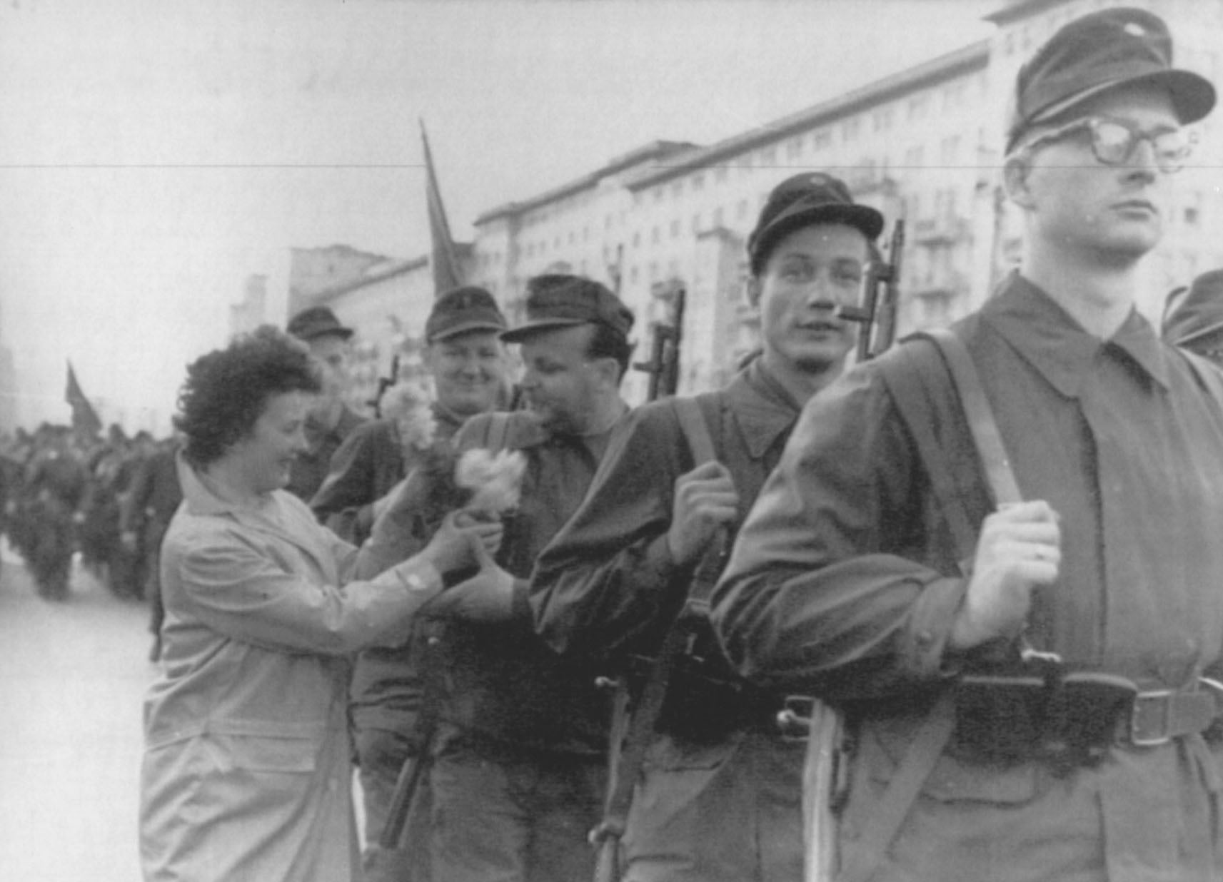 Mujer dando un ramo de flores a un miembro de las brigadas de la RDA dirigiéndose a la frontera.