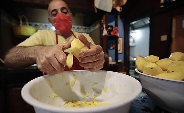Imagen principal - La tortilla de patatas paso a paso. Arriba, Ángel Galván corta las patatas a gran velocidad. Abajo, Tatyana Ivanova casca los huevos y, una vez batidos, los mezcla con la patata, previamnete frita. 