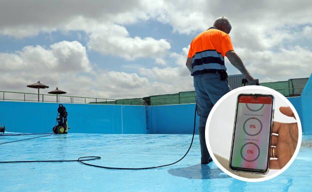 Un operario municipal realiza labores de limpieza en el vaso principal de la piscina de Rueda, que abrirá este verano. Abajo, aplicación en Tudela para informar del aforo. 