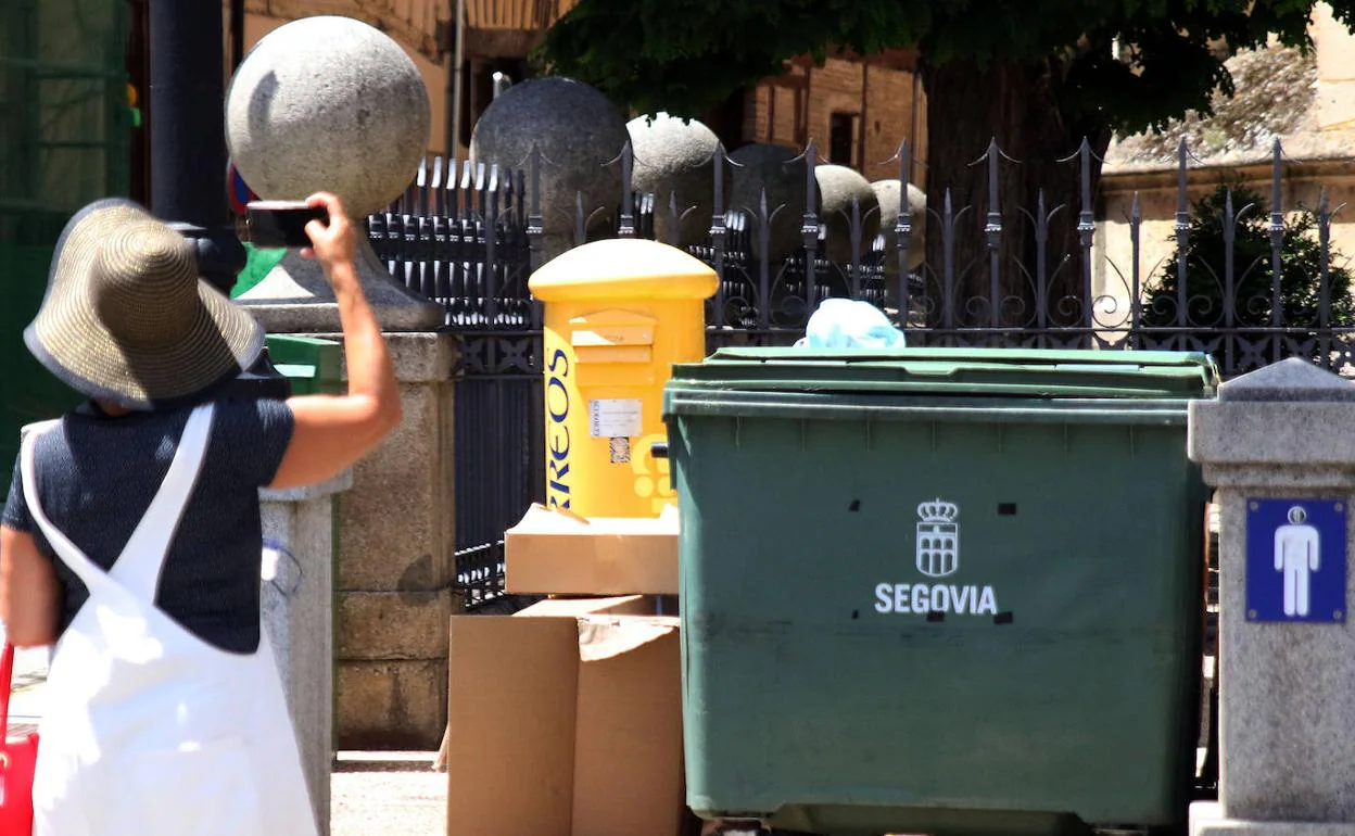 Una turista hace una foto a la Catedral de Segovia ante un contenedor y restos de cartón. 
