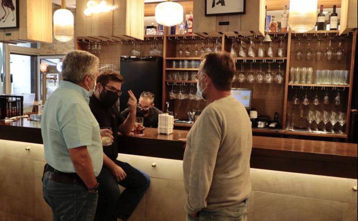 Tres clientes consumen ya en la barra de un bar. 