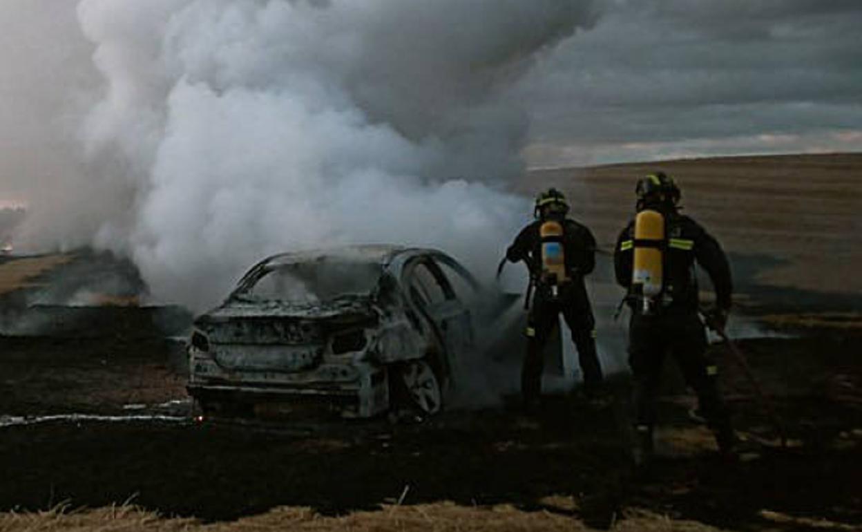 Bomberos y agentes forestales sofocan las llamas del BMW y de los rastrojos colindantes.