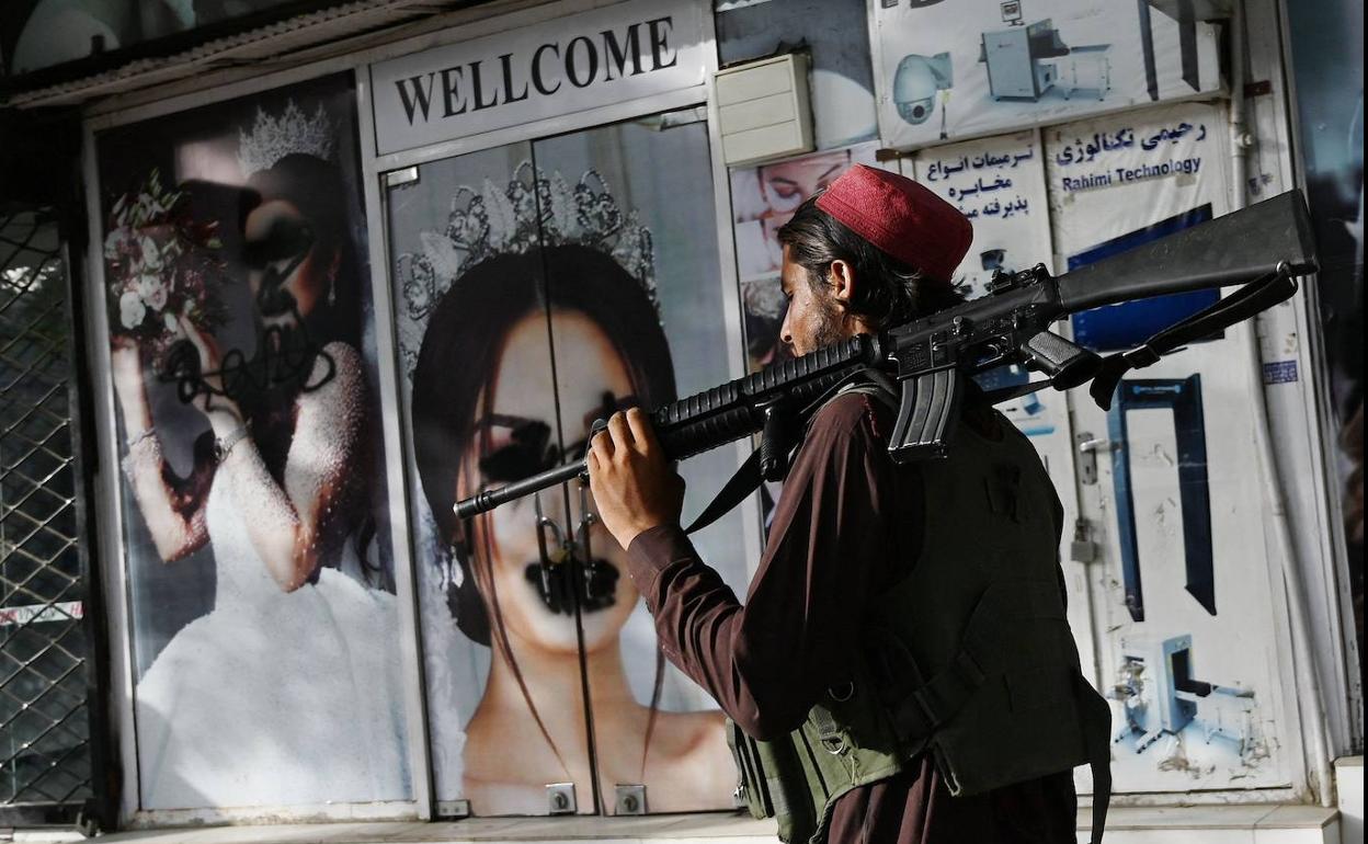 Un soldado talibán camina por las calles de Kabul frente a un salón de belleza con pintadas en las caras de las modelos.