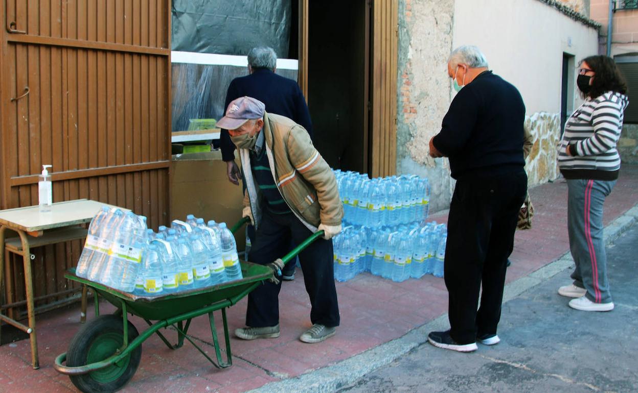 Un vecino de Lastras de Cuéllar porta una carretilla cargada con botellas, mientras otros tres personas esperan para recoger agua embotellada.