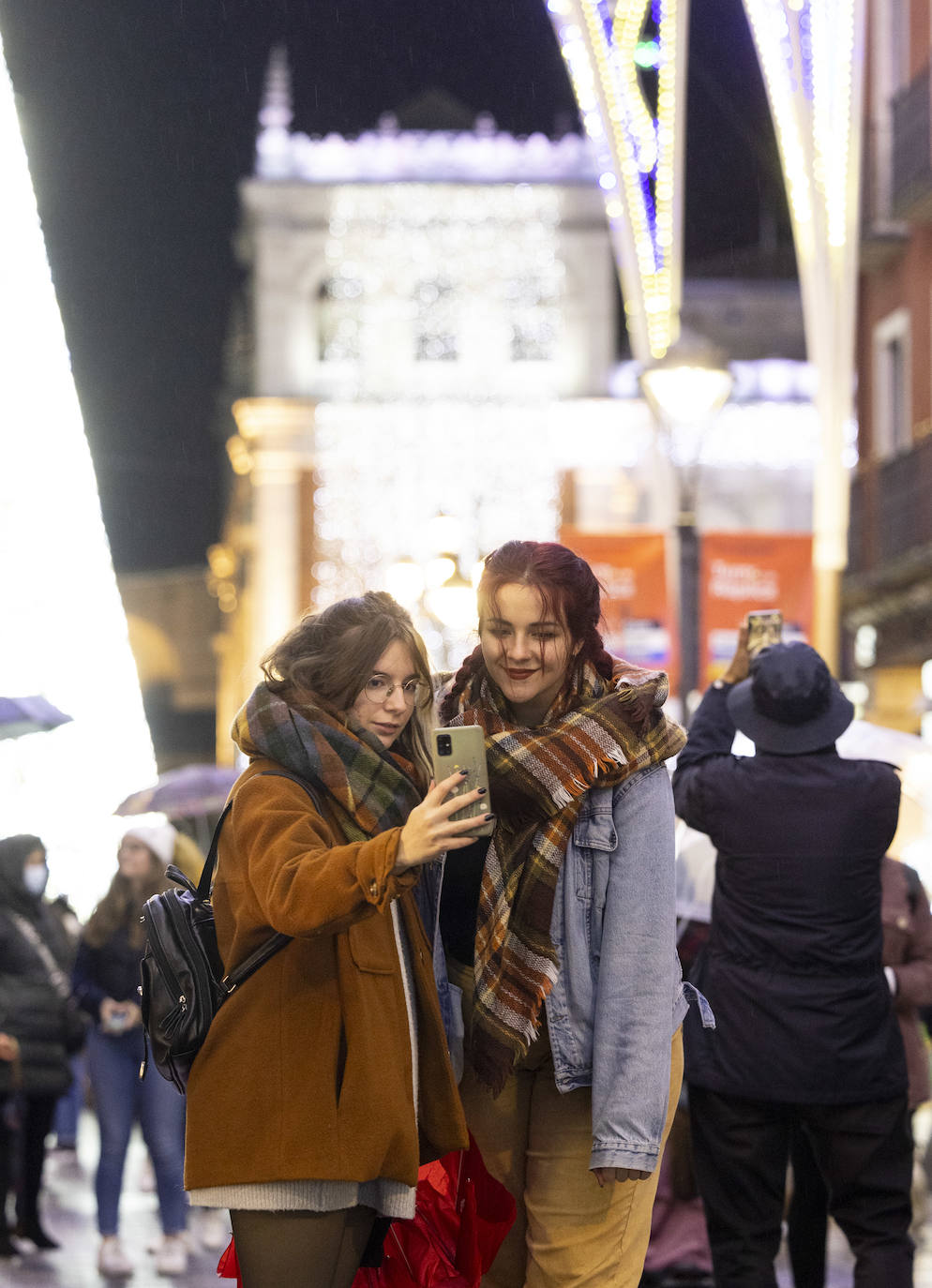 Dos jóvenes se hacen un selfie con las luces de la calle Santiago de fondo.