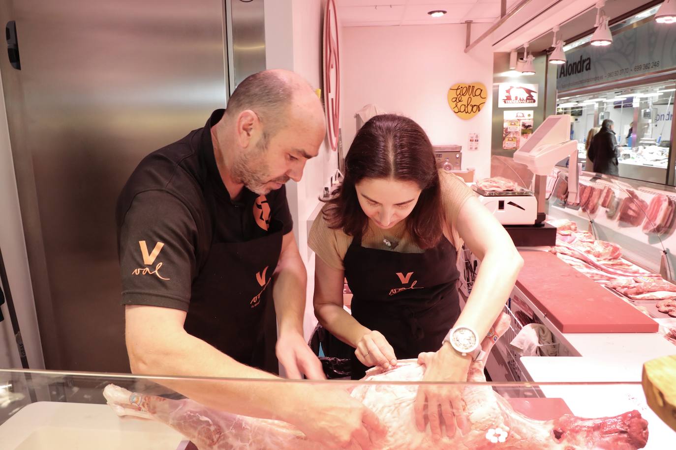 Imagen principal - Arriba, Elena Arzak se asoma a las entrañas del lechazo mientras Javier de la Heras le explica las partes con las que se hace la asadurilla. Abajo, prueba las pechugas escabechadas, en presencia de Esther Rodríguez y su hija, Parquel Mayo, y observa el producto de algunos puestos. 