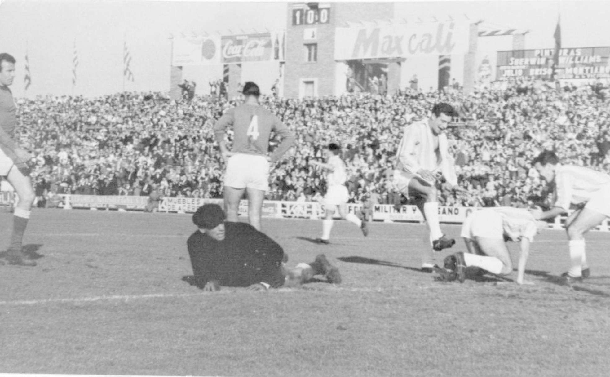 Aramendi y Mirlo abrazan alborozados a Morollón, autor del primer tanto blanquivioleta ante el Oviedo. Carlos Gomes, con su uniforme y gorra negros, no puede ocultar su decepción, mientras el encargado del marcador coloca el 1-0 