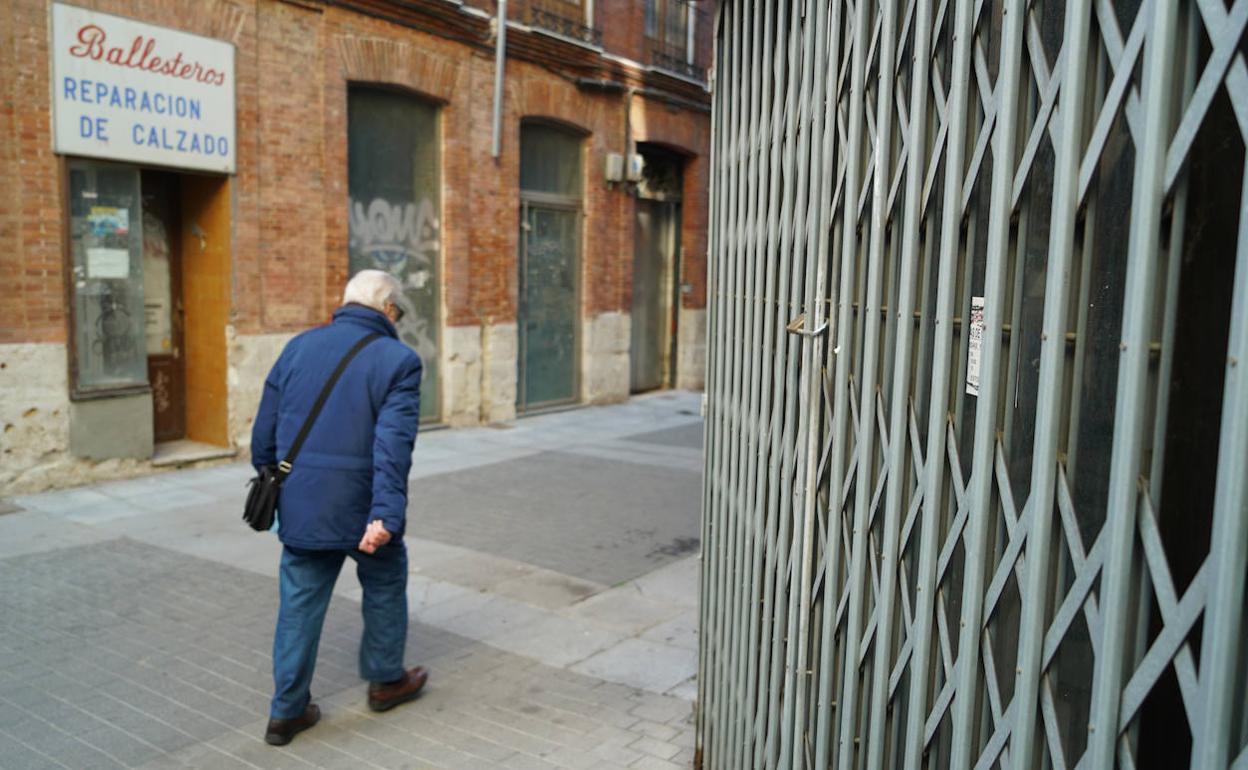 Un hombre pasa junto a una verja cerrada de un local en alquiler en Valladolid. 