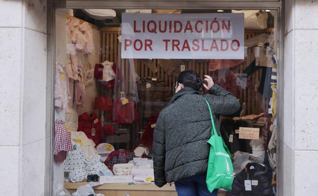 Una mujer mira el escaparate de una tienda en el que se anuncia la liquidación por traslado. 