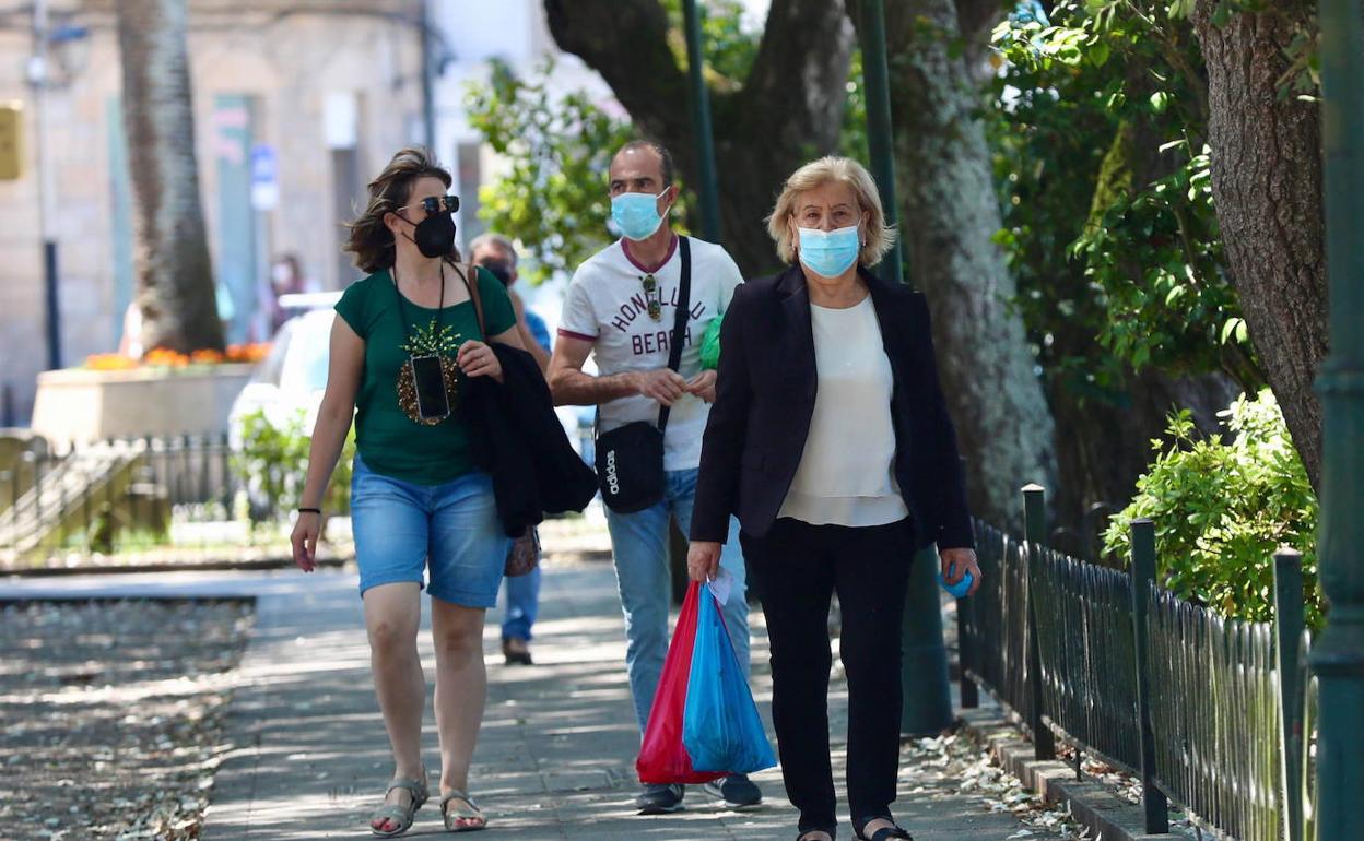 Unas personas pasean , en la calle con mascarilla. 