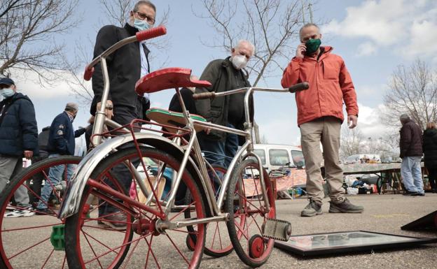 Tres hombres observan un par de triciclos antiguos en el rastro de Valladolid. 