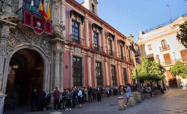 Decenas de fieles hacen cola ante el edificio del Arzobispado de Sevilla para acceder a la capilla ardiente.