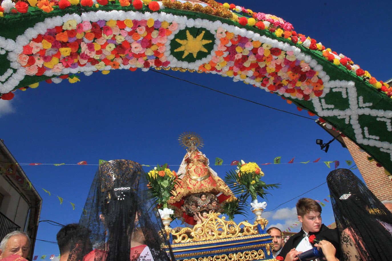 Los grupos de paloteo preceden el paso de la Virgen del Castillo por uno de los arcos de flores de papel en Bernardos. 