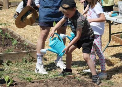 Imagen secundaria 1 - La monitora Lidya Martínez se dirige a los pequeños. Un niño riega las plantas. 