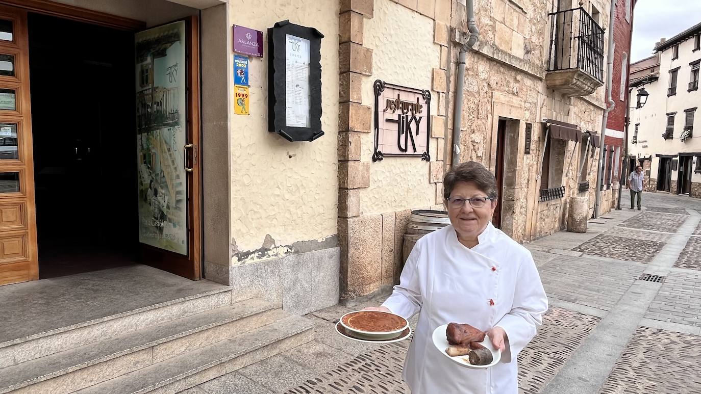 Imagen principal - Arriba, Mari Carmen Subiñas, responsable de cocina del restaurante Tiky, de Covarrubias, posa con una olla podrida. Abajo, las casas típicas del municipio y la Colegiata de San Cosme y San Damián. 