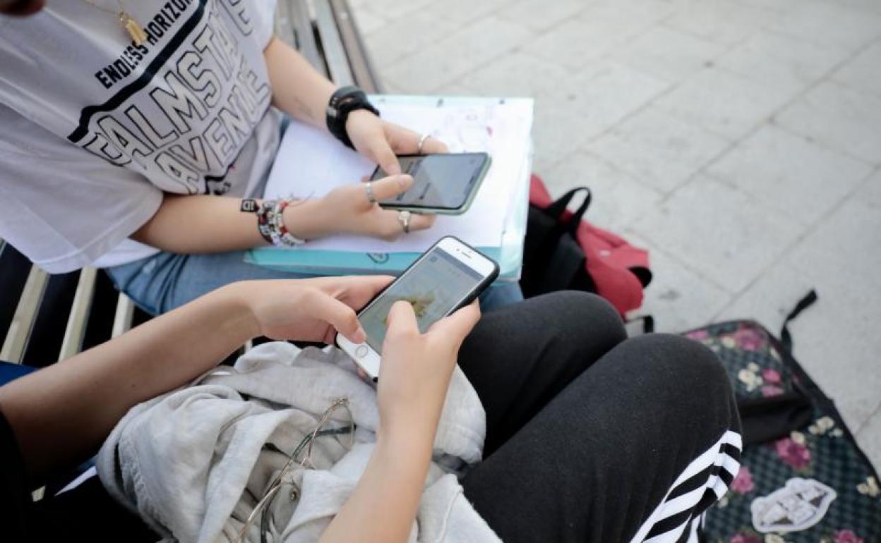 Dos jóvenes consultan contenido en sus teléfonos móviles. 