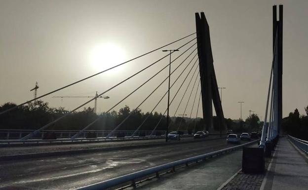 Tráfico en el Puente de la Hispanidad con el sol semioculto entre la calima. 