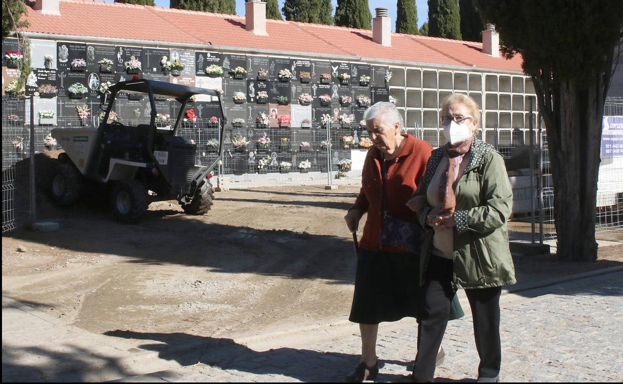 Dos mujeres pasan por uno de los patios del cementerio con una máquina de obras al fondo. 