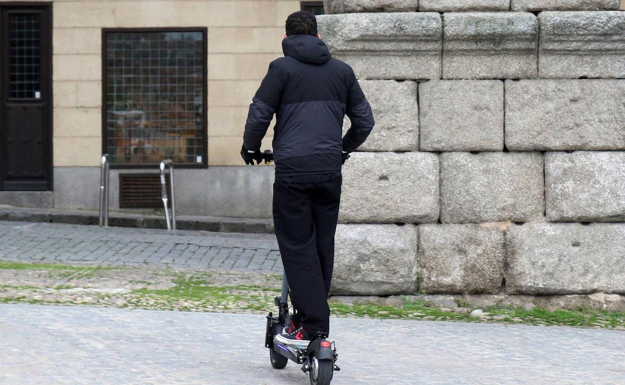 Un joven monta en patinete en una zona peatonal, junto al Acueducto de Segovia. 