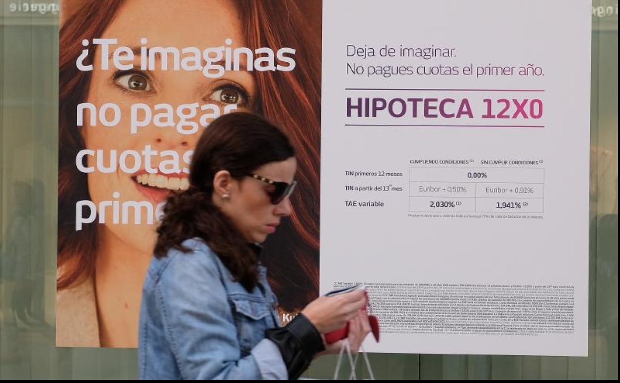 Una viandante cruza frente al escaparate de un banco con un anuncio publicitario de hipotecas.