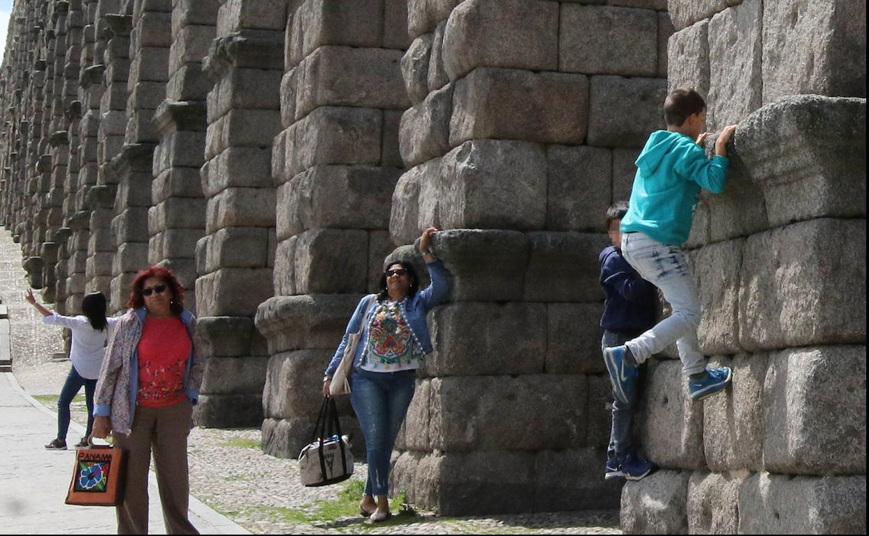 Dos niños escalan por el Acueducto mientras una mujer se apoya en el monumento. 