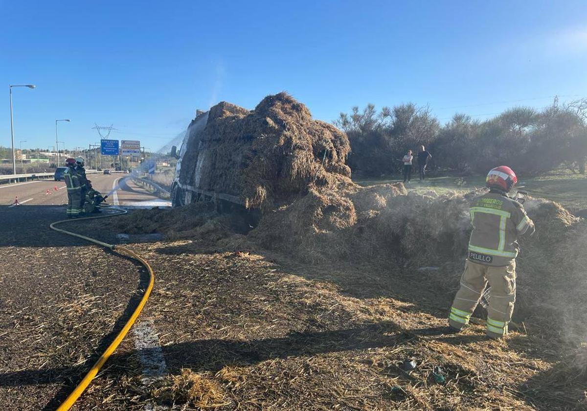 Efectivos de los bomberos sofocan el incendio en el camión cargado de paja.